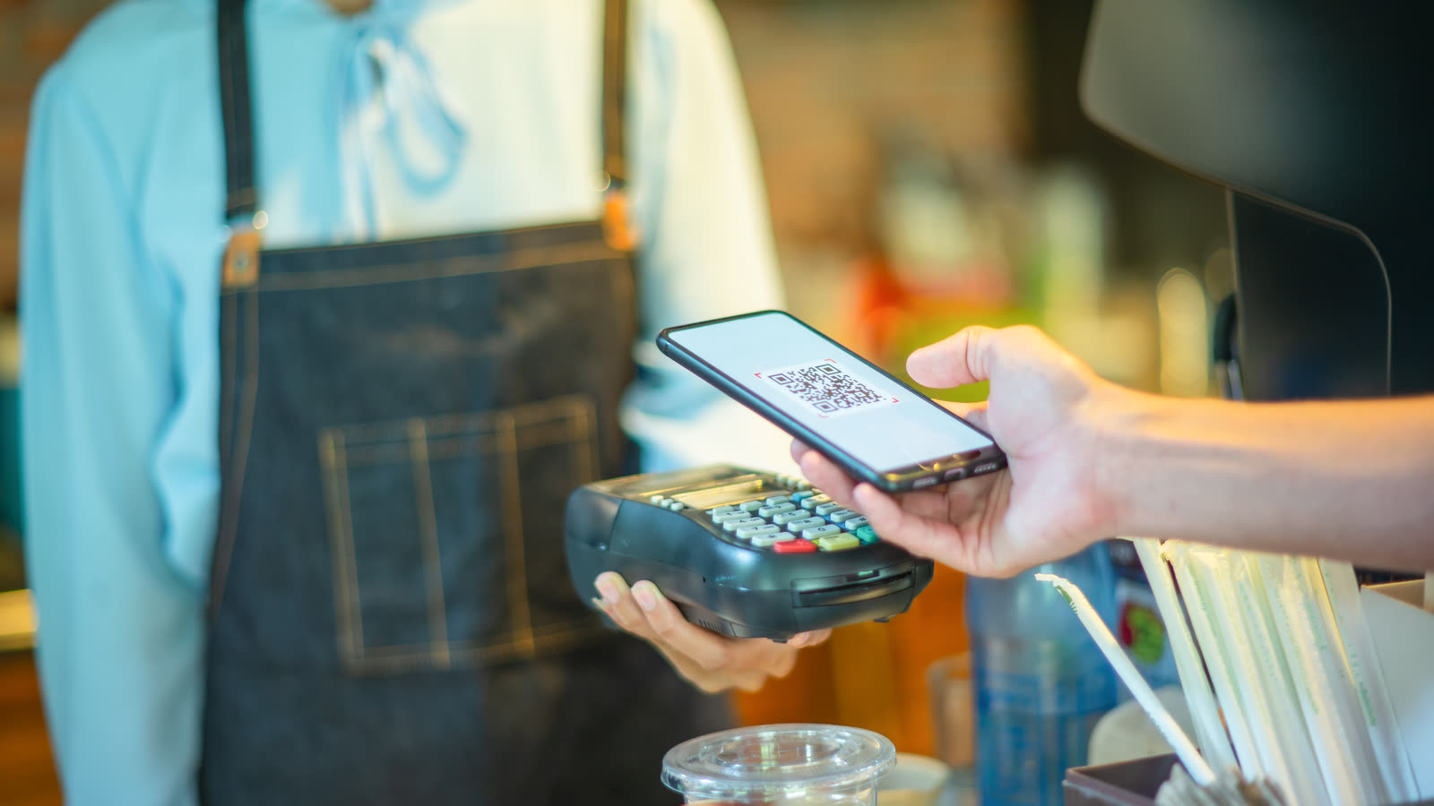 A customer pays by scanning a QR code with a smartphone at a payment terminal