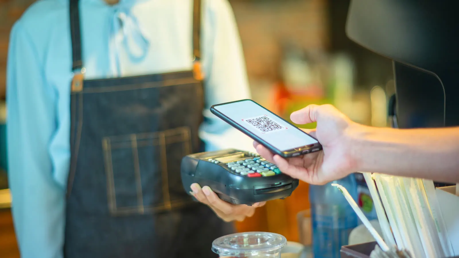 A customer pays by scanning a QR code with a smartphone at a payment terminal